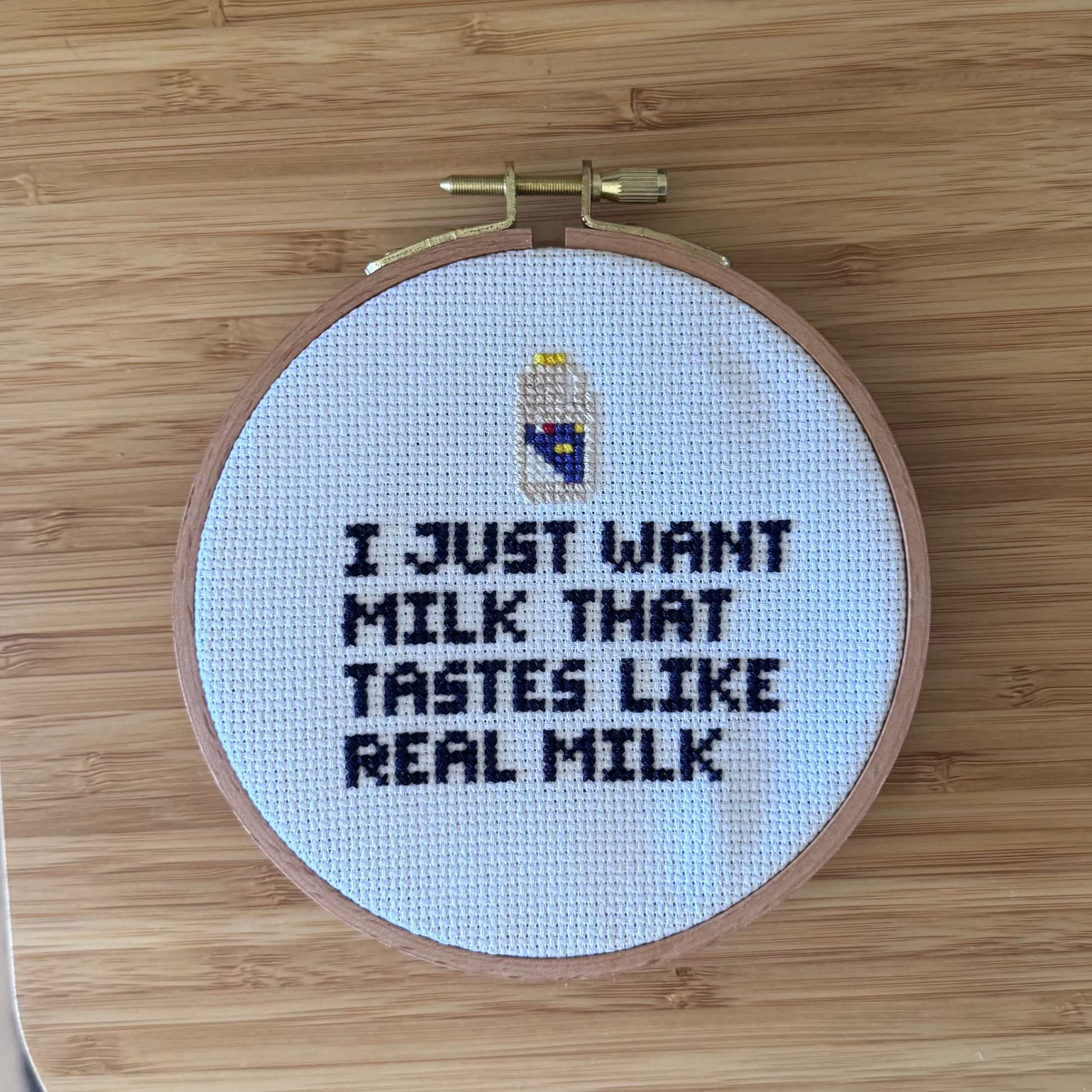 Embroidery hoop with cross-stitched text on a wooden surface with words from a milk ad 